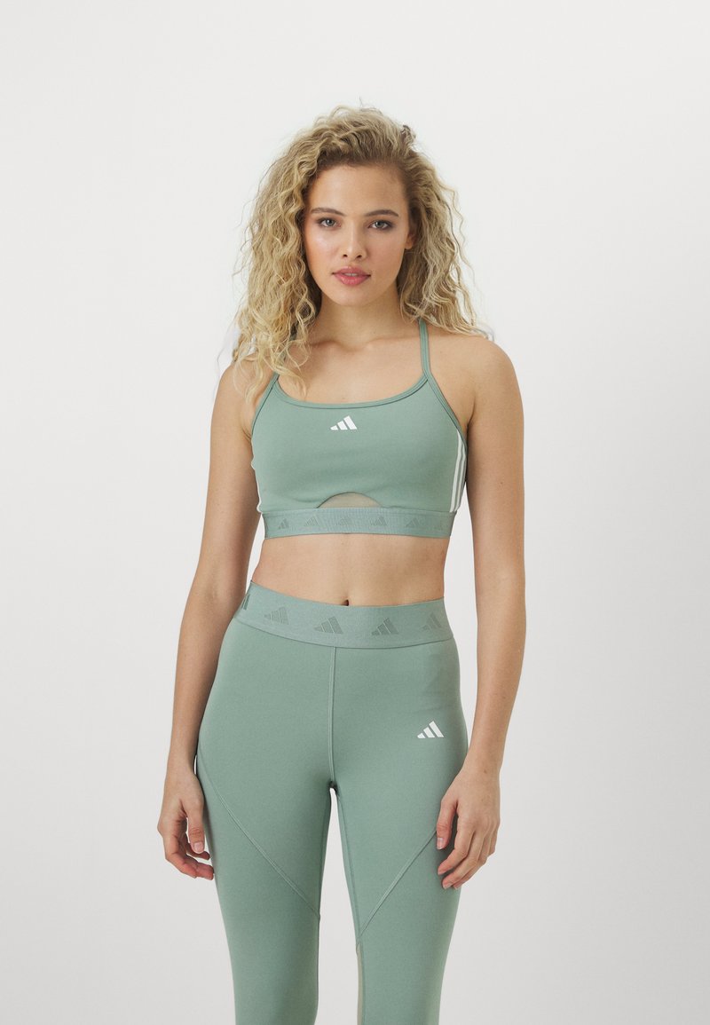 Top deportivo verde de corte corto con tirantes finos y detalles recortados, combinado con leggings de cintura alta a juego que presentan acentos texturizados y un logo.