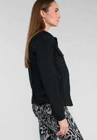 Zwarte spijkerjasje met een aansluitend ontwerp, knoopsluiting en twee borstzakken. Gecombineerd met zwart-witte broek met patroon.