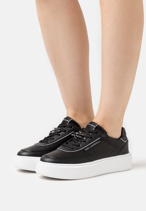 Schwarze Ledersneaker mit weißer Gummisohle, metallischen Schnürsenkeln und einem dezenten Logo an der Seite, mit schimmernden Akzenten an der Ferse.