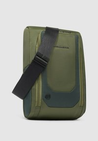 Borsa a tracolla verde oliva in tessuto texturizzato, con cuciture rinforzate e tracolla nera regolabile. Dotata di una tasca con cerniera e dettaglio con logo.