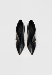 Μαύρα δερμάτινα παπούτσια με ψηλό τακούνι και μυτερή μύτη, με κλειστή μύτη και χρυσή λεπτομέρεια στο μπροστινό μέρος. Ομαλή υφή.
