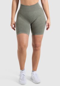 Hooggesneden olijfgroene atletische shorts van textiel. Heeft een zachte afwerking en een geribde tailleband. Gekocht met witte sneakers.