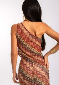 Vestido asimétrico con una tela texturizada y un patrón geométrico en tonos cálidos de rojo, marrón y beige. Fondo blanco.