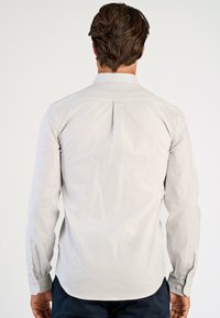 Ριγέ πουκάμισο με κουμπιά σε ανοιχτό γκρι και λευκό. Διαθέτει μακριά μανίκια, πλάτη με πιέτα και μανσέτες με κουμπιά. Βαμβακερό ύφασμα με διακριτική υφή.