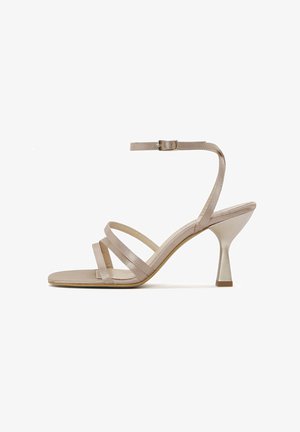 Beige strappy high-heeled sandal with a metallic heel, featuring three narrow straps across the foot and an ankle buckle closure.