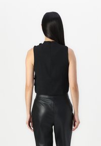 Top negro sin mangas con tejido texturizado, cuello alto, cierre de botón en la parte posterior y combinado con pantalones de cuero negro.