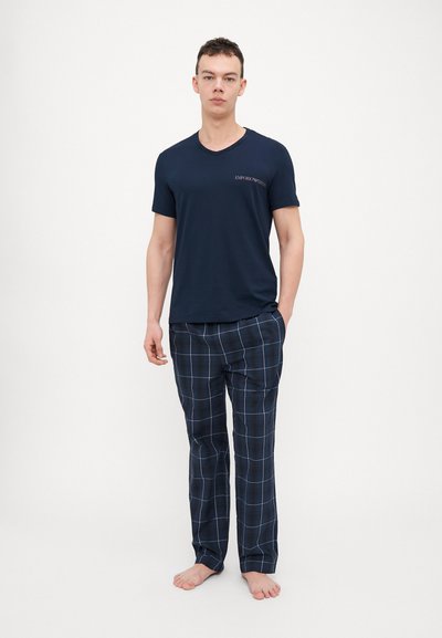 Marineblauwe V-hals T-shirt gecombineerd met geruite loungebroek in marineblauw en wit. Katoenmengsel, ontspannen pasvorm, met zichtbare branding op het shirt.
