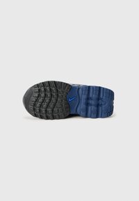 Semelle de chaussure de sport noire et bleue avec une surface en caoutchouc texturée, des motifs circulaires et carrés, et un accent du logo Nike en bleu.