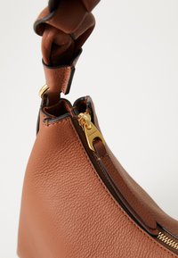 Brown textured leather handbag with braided handle and gold zipper detail against a white background.