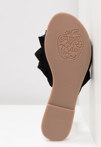 Svart tygsko med en texturerad sula, med en volangdetalj längs sidan och präglad "Apple of Eden"-logotyp på botten. Storlek 37.