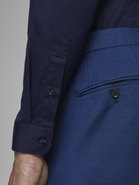 Navy shirt with buttoned cuffs paired with blue textured trousers; visible stitching details and buttons on the shirt sleeve and pants.