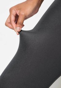 Tight neri elasticizzati tirati da una mano, che mostrano una superficie liscia e un motivo a costine. Il tessuto appare morbido ed elastico.