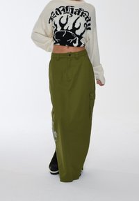 Olivengrøn maxi-nederdel med sidelommer, der har en høj slids og blomsterbroderi, parret med en cropped sweater med fed tekst.