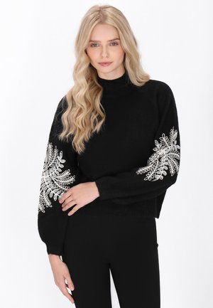 Zwarte trui met lange mouwen, versierd met ingewikkelde zilveren bloemenborduursels op de manchetten. Géhaakt materiaal met een hoge kraag en een cropped ontwerp.