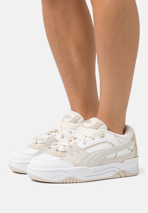 White and beige sneakers with a mix of smooth synthetic and textured suede materials, round toe, and lacing system, featuring a brand logo on the tongue.