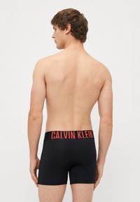 Boxeri negri din bumbac cu un brâu elastic lat, având textul contrastant "CALVIN KLEIN" în roșu. Material moale, se potrivesc bine, lungime până la mijlocul coapsei.