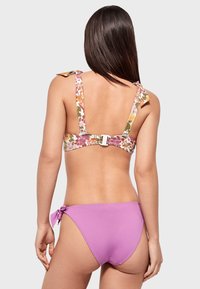 Bikini de dos piezas con un top de estampado floral y tirantes ajustables, y una parte inferior lisa en lavanda con un lazo en el costado. Fabricado con tejido de baño.