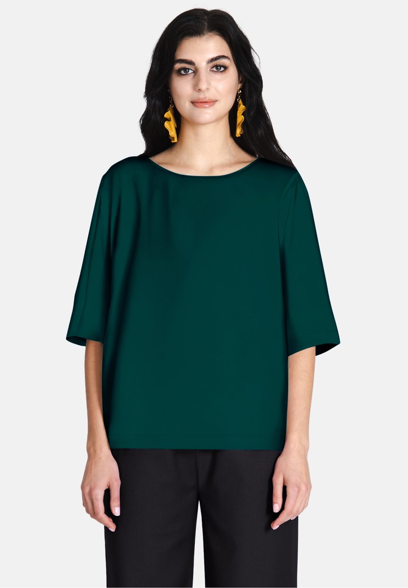Top corto color teal con scollatura ampia e vestibilità comoda. Il tessuto ha una trama liscia, abbinato a pantaloni scuri a vita alta.