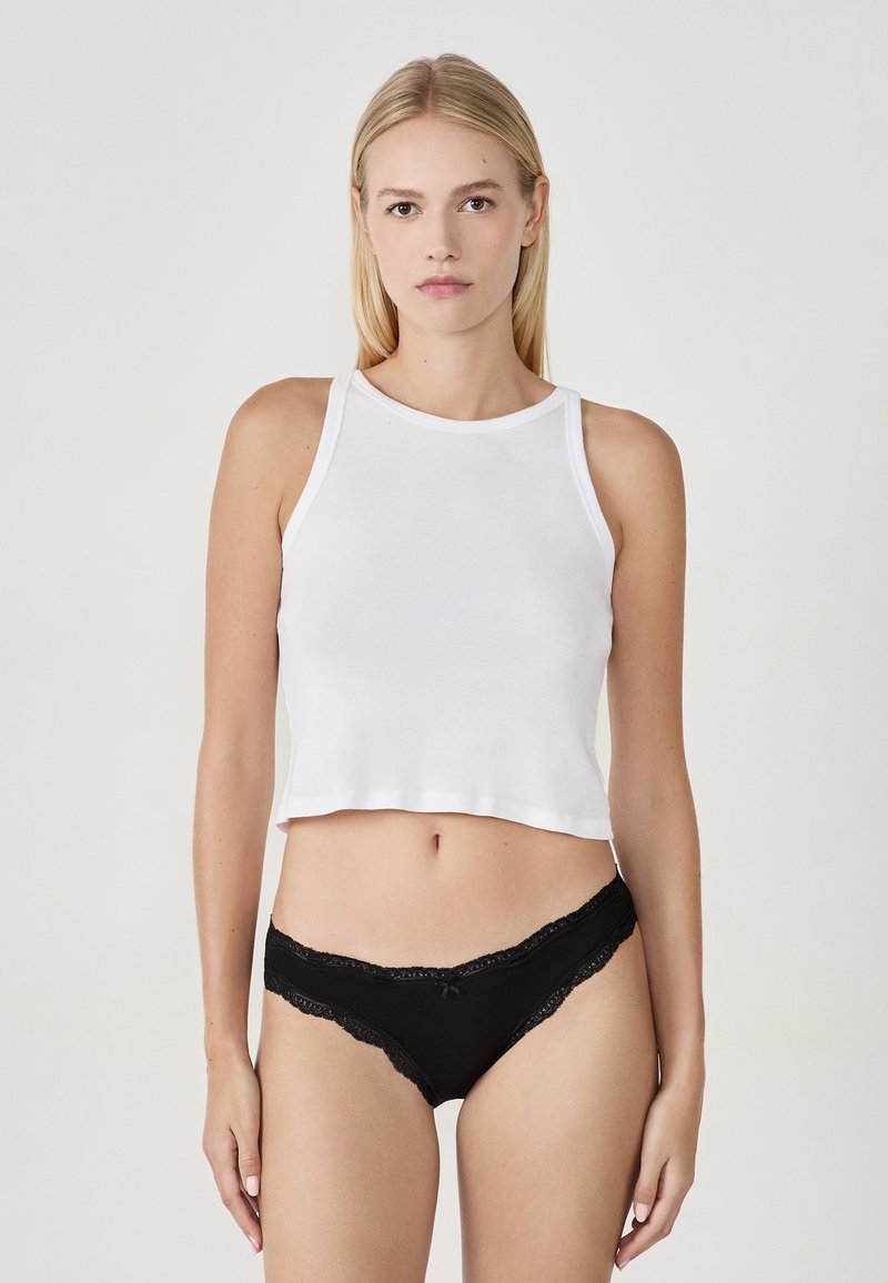 Débardeur blanc court avec un col rond, associé à une culotte noire ornée de dentelle et d'un petit noeud. Texture en coton doux.