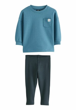 Blaues Baumwoll-Sweatshirt mit einer Brusttasche und gerippten Bündchen, kombiniert mit dunkelgrauen gerippten Leggings. Beide haben eine weiche Textur.