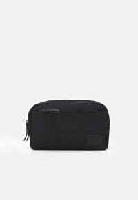 Pochette noire avec une texture lisse et mate, de forme rectangulaire et une fermeture éclair en haut. Présente un petit logo en relief sur le côté.