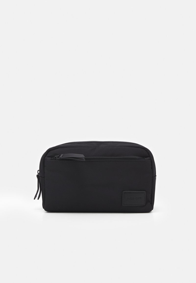 Pochette noire avec une texture lisse et mate, de forme rectangulaire et une fermeture éclair en haut. Présente un petit logo en relief sur le côté.