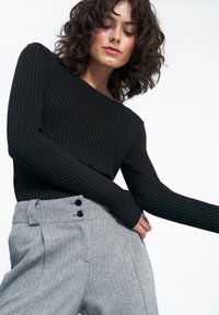 Czarny, prążkowany, długi rękaw top zestawiony z szarymi spodniami w wzór houndstooth z podwójnymi czarnymi guzikami w talii. Gładka tekstura i dopasowany krój.