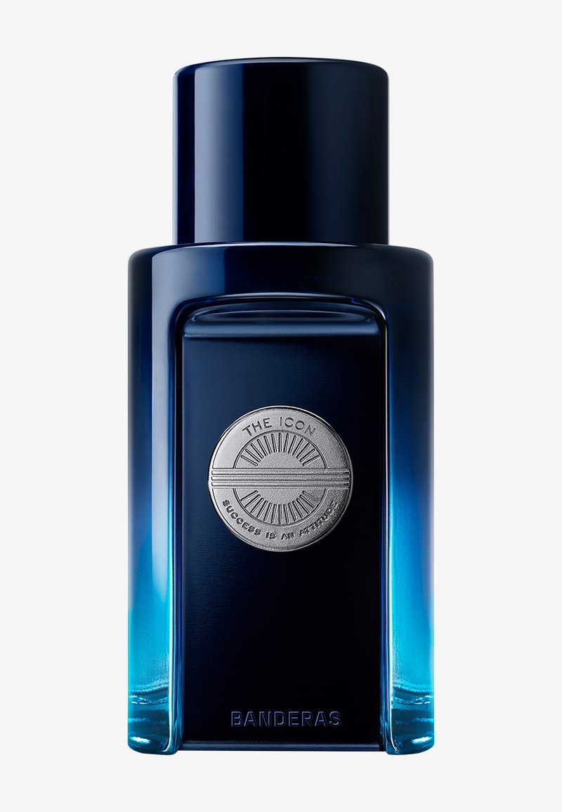 Høj rektangulær mørkeblå parfume flaske med et rundt sølvemblem og ordet "Banderas" ved bunden.