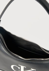 Μαύρη δερμάτινη τσάντα χειρός με ομαλή υφή, που διαθέτει επάνω φερμουάρ κλεισίματος και ασημένιο τράβηγμα φερμουάρ. Το εσωτερικό είναι επενδεδυμένο με μαύρο ύφασμα.