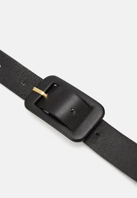 Musta nahkahihna, jossa on teksturoitu pinta, varustettuna suorakulmaisella metallisoljella mustana ja kultaisena, sekä useilla säätörei'illä.