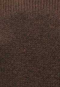 Nahaufnahme von strukturiertem dunkelbraunem Strickstoff mit einem vertikalen Rippmuster und leicht flauschigen Zwirnfäden.