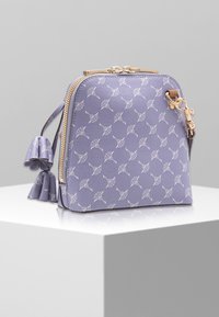 Fioletowa torba z fakturowanej skóry z białym wzorzystym wzorem, zamknięciem na zamek i złotymi okuciami. Zdobiona dekoracyjnym chwostem w kształcie kokardy.