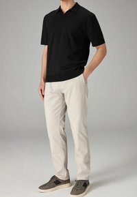 Polo noir à manches courtes avec une texture en maille subtile, associé à un chino beige clair et des baskets grises avec des accents foncés.