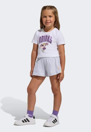 Biele tričko s krátkym rukávom s fialovým nápisom "ADIDAS" a postavičkou, v kombinácii so sivými šortkami. Model má na sebe biele tenisky s čiernymi pruhmi.