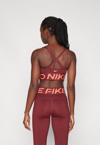 Bordo športni modrček s križnimi naramnicami in Nike logotipom. Ujemajoče se bordo legice s kontrastnim oranžnim besedilom "NIKE" na pasu.