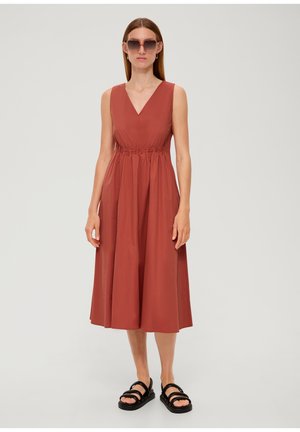 Rostfarbendes Midi-Kleid für Frauen mit V-Ausschnitt, elastischem Taillenbund und schwingendem Rock. Getragen mit schwarzen Riemchensandalen und übergroßen Sonnenbrillen.