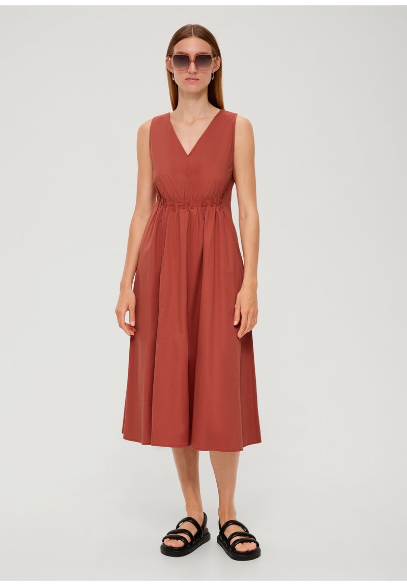 Roestkleurige midi-jurk voor dames met een V-hals, elastische tailleband en een vloeiende rok. Draagt u met zwarte sandalen met banden en oversized zonnebril.