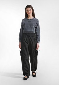 Grå cropped sweatshirt med "DEHA" logo, kombineret med sorte letvægts cargo bukser med mesh sidelommer og elastiske manchetter. Sorte sko.