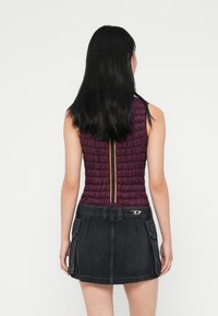 Κουβερλί σε μπορντό, χωρίς μανίκια, με κίτρινο φερμουάρ, σε συνδυασμό με μαύρη τζιν φούστα με τσέπες και διακοσμητική μεταλλική λεπτομέρεια.