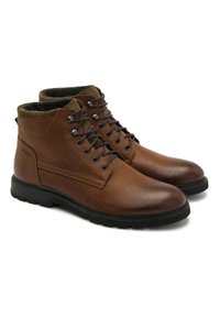 Brązowe skórzane botki za kostkę z czarnymi gumowymi podeszwami, zaokrąglonymi noskami i metalowymi oczkami na sznurówki. Fleece na górze dodaje faktury i ciepła.