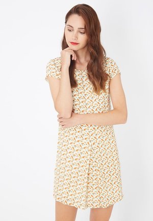 Vestido de tela ligera y manga corta en color crema con un patrón colorido de formas naranjas y azules, que presenta un ajuste relajado y un dobladillo a la altura de la rodilla.