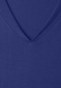 Nahaufnahme von tiefblauem Stoff mit V-Ausschnitt-Nahtdetail auf einer weichen, glatten Textiloberfläche.