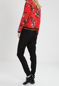 Czerwony sweter z kwiatowym wzorem, z czarnym pasem w talii, w zestawieniu z czarnymi dopasowanymi spodniami i czarnymi butami. Projekt charakteryzuje się żywymi kolorami i skomplikowanymi wzorami.