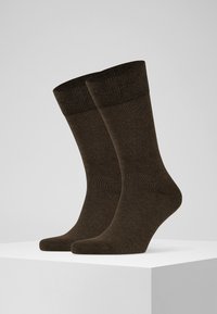 Brown socks made of soft, textured fabric. Features a ribbed cuff and smooth body. Displayed upright on a white pedestal against a gray background.