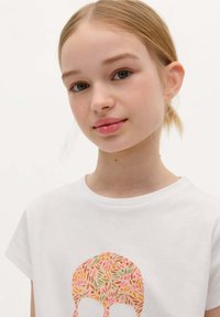 White short-sleeve t-shirt featuring a colorful skull design made of leaf patterns in pink, orange, and green hues.