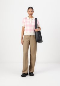 Strikket kortermet polo skjorte i rosa og hvit rutemønster, sammen med beige vide bukser og en svart skulderveske.