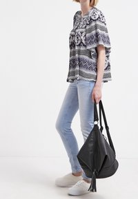 Blusa a righe bianco e nero con maniche ampie, abbinata a jeans skinny azzurri e sneakers bianche. Borsa nera morbida con dettaglio a frangia.