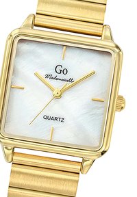 Montre en quartz carrée dorée avec un cadran en nacre blanche, logo noir, aiguilles dorées et bracelet en or texturé.