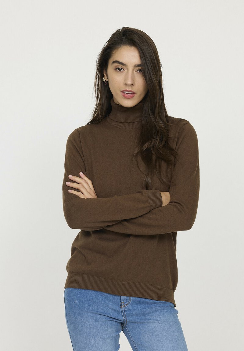 Pull en col roulé marron avec des détails côtelés au col et aux poignets, associé à un jean bleu, présenté sur un fond neutre.