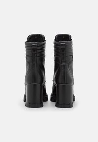 Botas de cuero negras hasta el tobillo con un alto tacón de bloque, detalles acolchados en la parte superior y una cremallera trasera. Textura suave con un diseño robusto.
